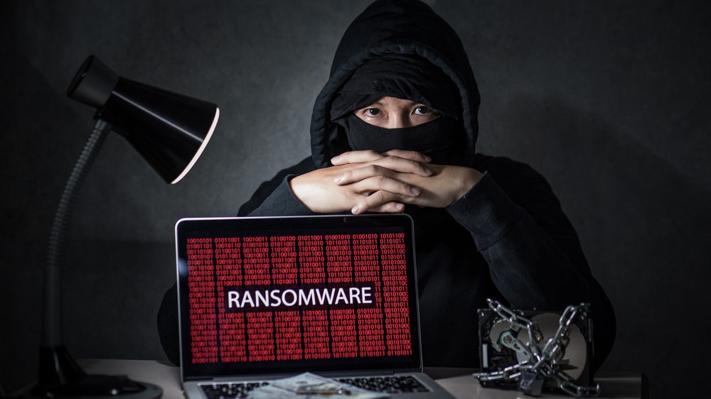 Masked hacker behind laptop displaying ransomware attack and binary code